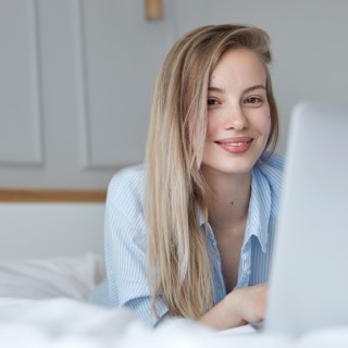 Beautiful young woman relaxing on bed with laptop